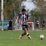 Jogadores adolescentes disputam uma partida de futebol em um campo gramado ao ar livre.