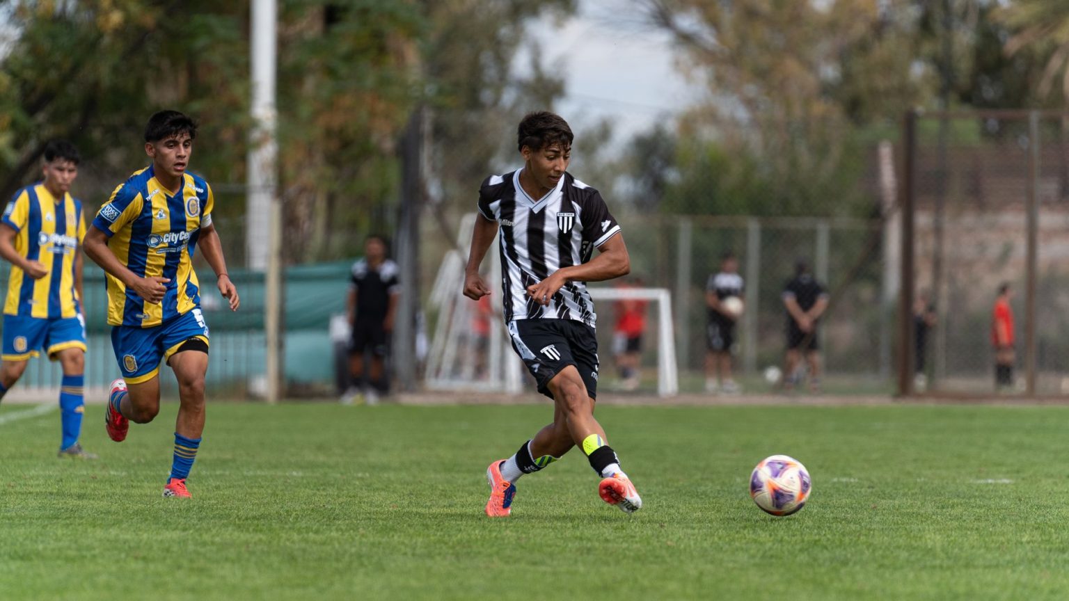 Jogadores adolescentes disputam uma partida de futebol em um campo gramado ao ar livre.