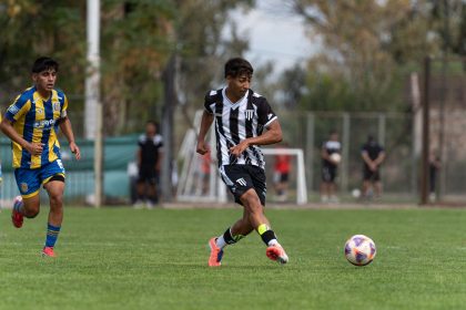 Jogadores adolescentes disputam uma partida de futebol em um campo gramado ao ar livre.