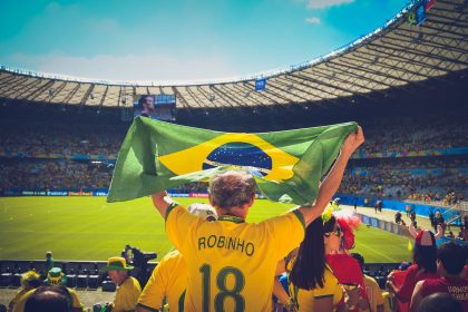 Torcedores brasileiros seguram uma bandeira do Brasil e comemoram nas arquibancadas de um estádio de futebol.