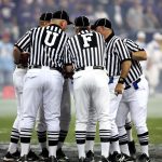 Grupo de oficiais de arbitragem conversa no campo de futebol.