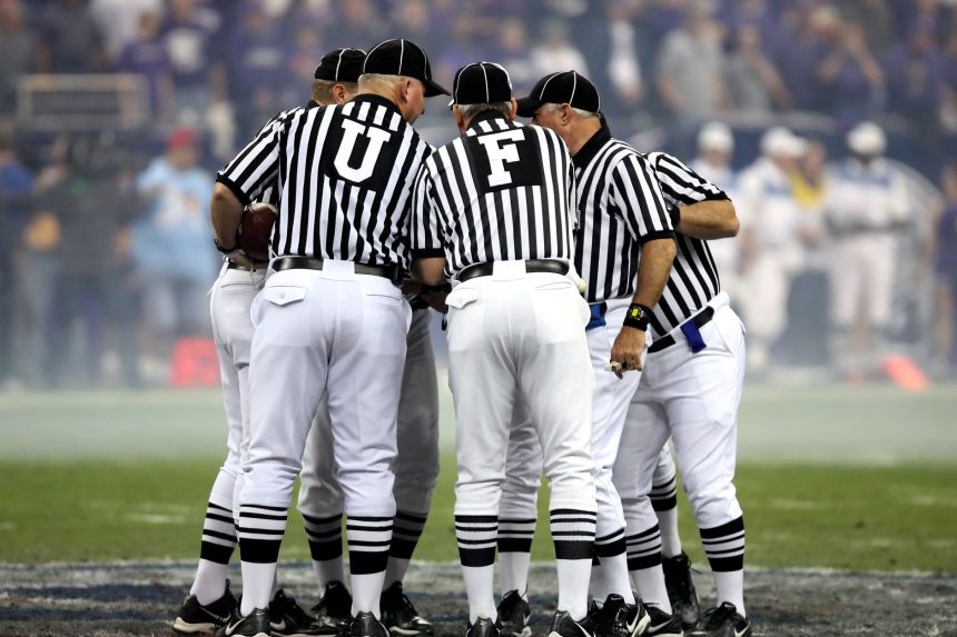Grupo de oficiais de arbitragem conversa no campo de futebol.