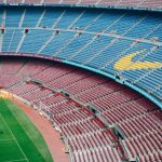 Vista aérea do estádio Camp Nou, em Barcelona, com arquibancadas coloridas e gramado vazio
