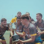 Equipe de futebol comemora a conquista de um título no campo, erguendo o troféu.