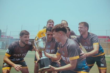 Equipe de futebol comemora a conquista de um título no campo, erguendo o troféu.