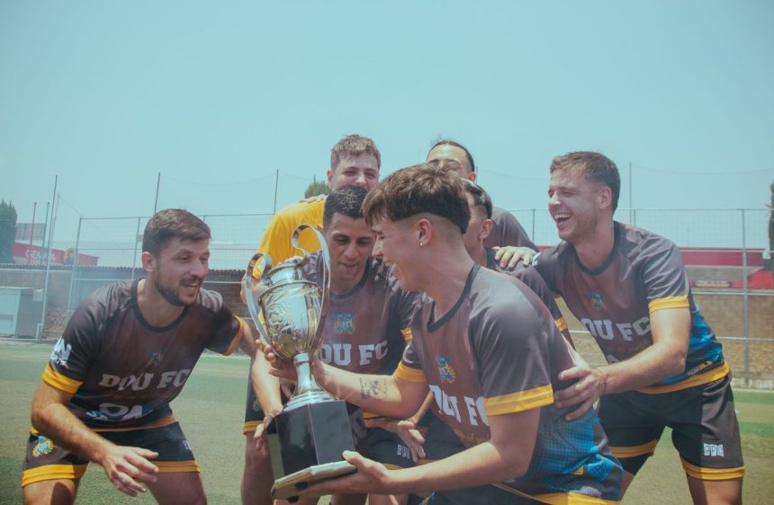 Equipe de futebol comemora a conquista de um título no campo, erguendo o troféu.
