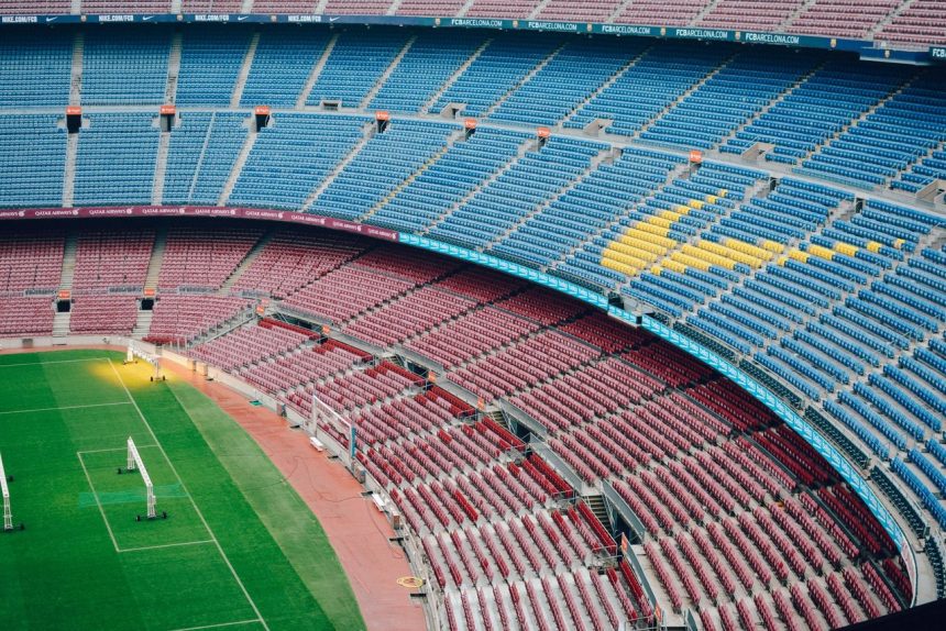 Vista aérea do estádio Camp Nou, em Barcelona, com arquibancadas coloridas e gramado vazio