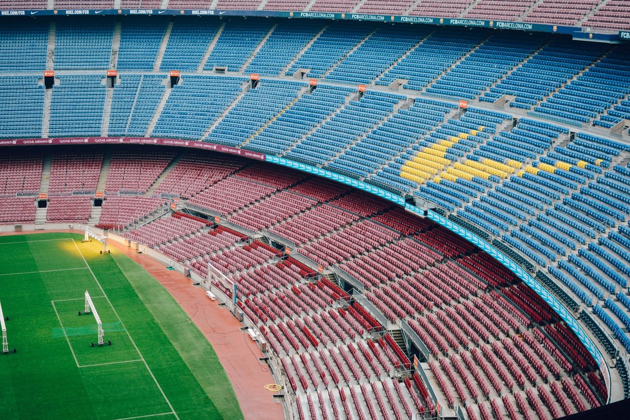 Vista aérea do estádio Camp Nou, em Barcelona, com arquibancadas coloridas e gramado vazio