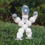 Robô humanoide de brinquedo sobre a grama, em um cenário relacionado ao futebol e à robótica.