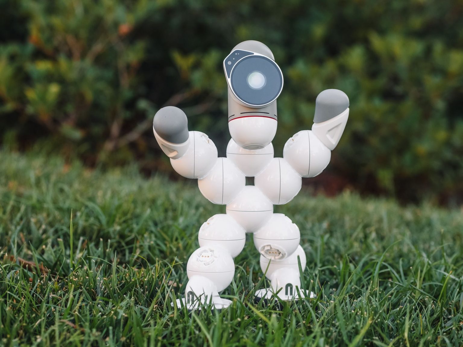 Robô humanoide de brinquedo sobre a grama, em um cenário relacionado ao futebol e à robótica.