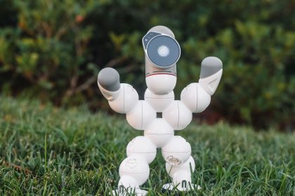 Robô humanoide de brinquedo sobre a grama, em um cenário relacionado ao futebol e à robótica.