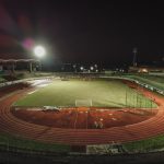 Vista aérea noturna do Estádio Willie Davids, com o campo de futebol iluminado e a pista ao redor.