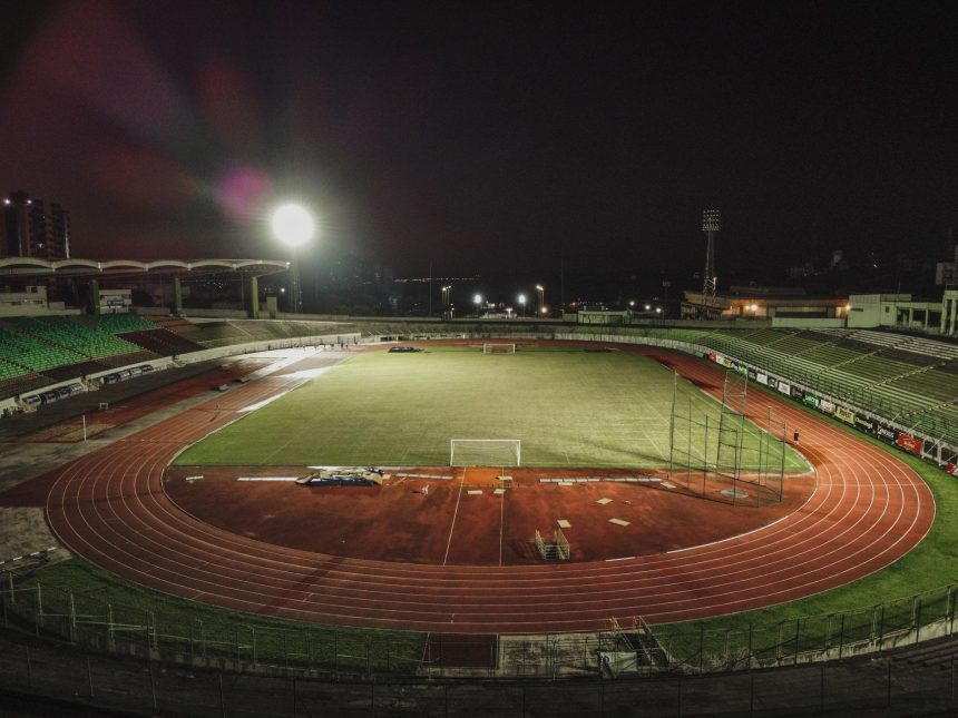 Vista aérea noturna do Estádio Willie Davids, com o campo de futebol iluminado e a pista ao redor.